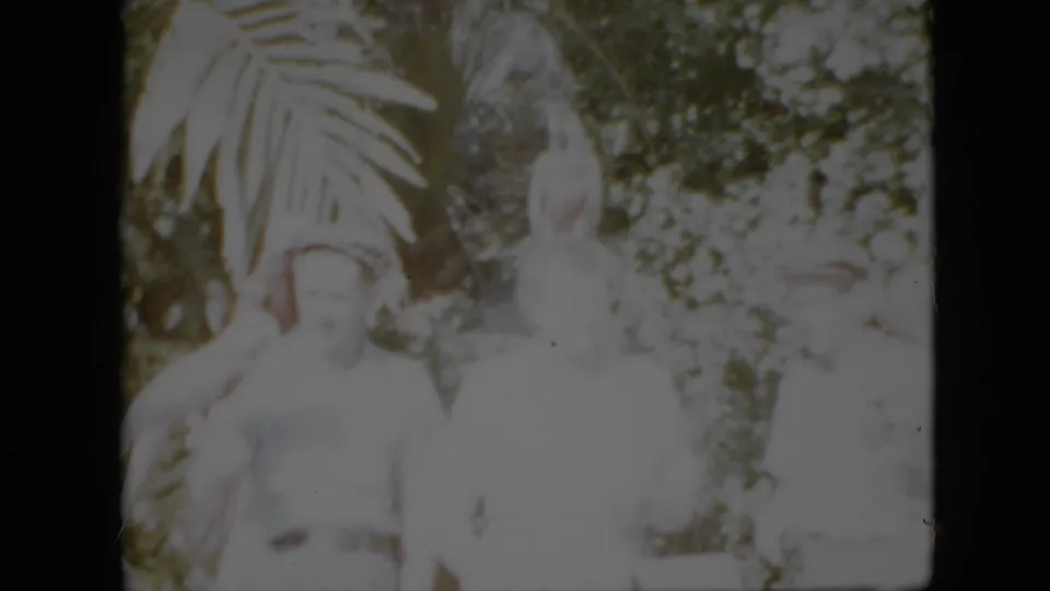 1958 Pennsylvania home-movie frame of adults posing in bright outdoor light, with a white parrot near a man and tropical foliage in the background.