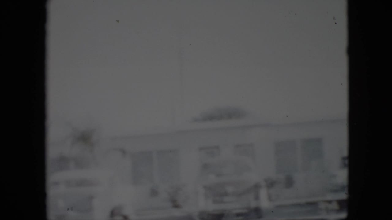 Parked cars in front of a low building seen through a dark 8mm frame border.