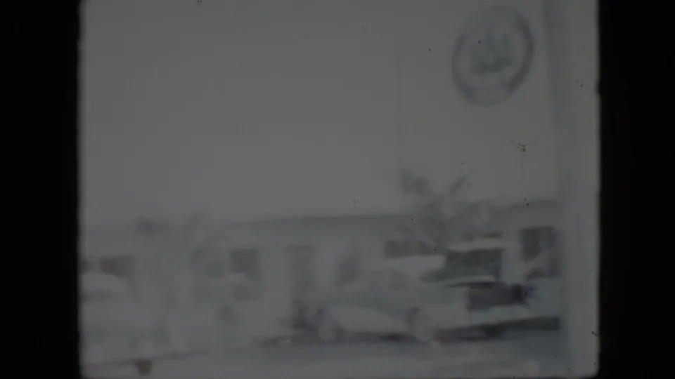 Soft 1958 Pennsylvania 8mm frame showing a parked automobile beside a low building and a faint circular sign-like shape in the upper area.