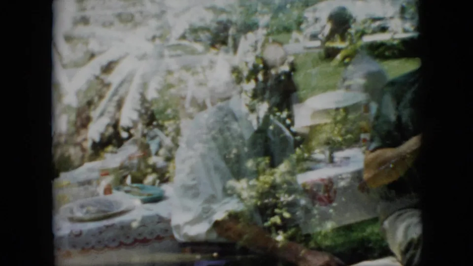 Pennsylvania 1958 frame of a family picnic scene, with adults gathered around a lace-covered table in a grassy yard and a standing figure partly visible at right.