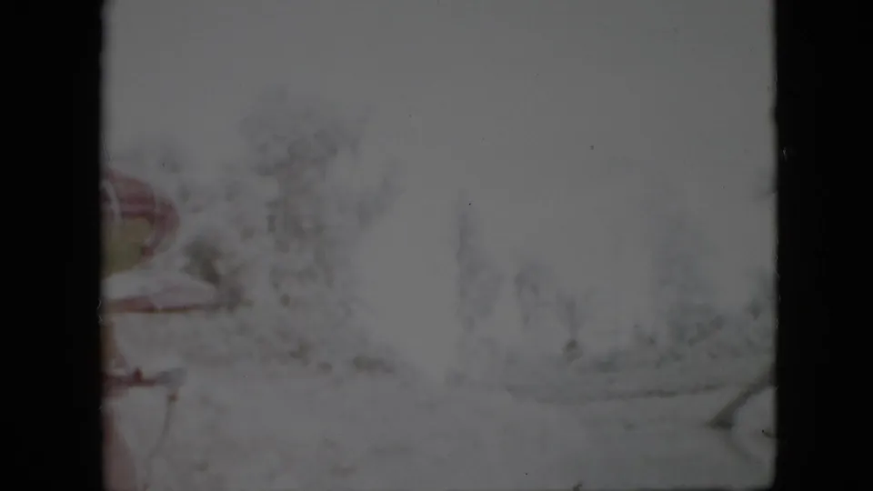 1958 Pennsylvania 8mm frame showing a low-contrast snowy landscape with blurred foliage, subdued color, and a faint curved edge near the ground.