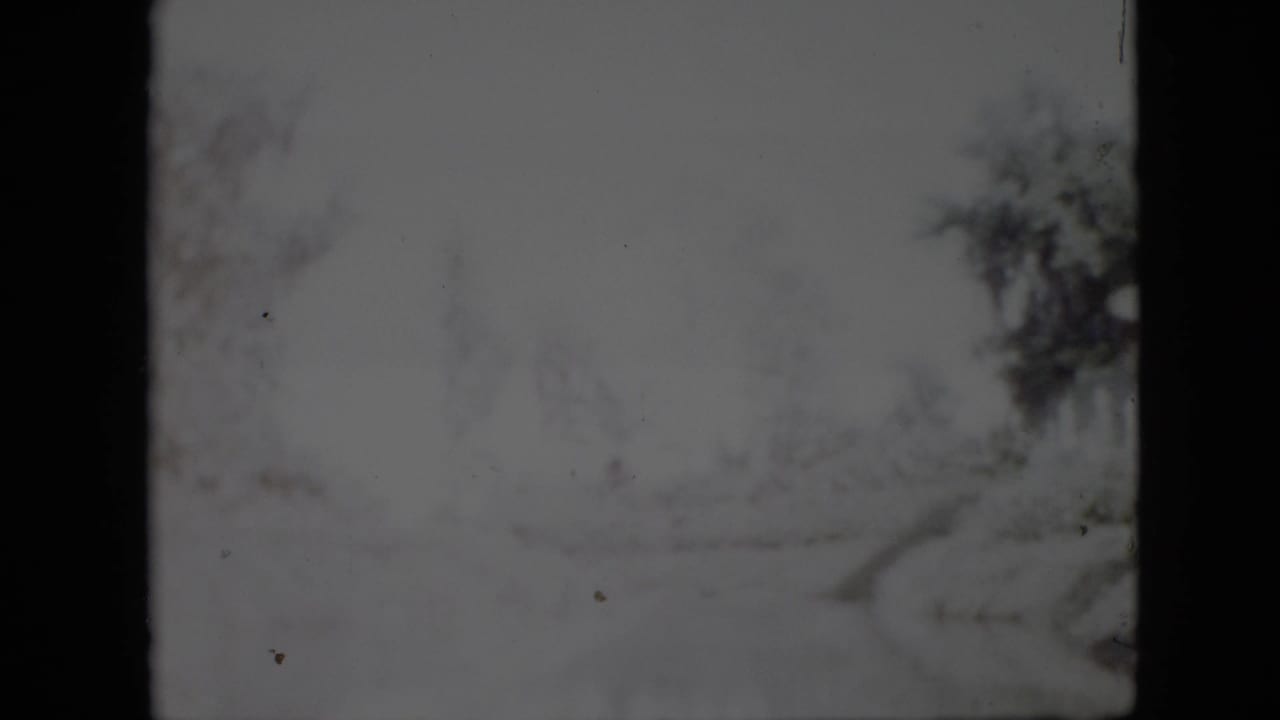 Soft 1958 Pennsylvania winter frame with a pale snow-covered path, leafless trees, and visible 8mm film gate edges.