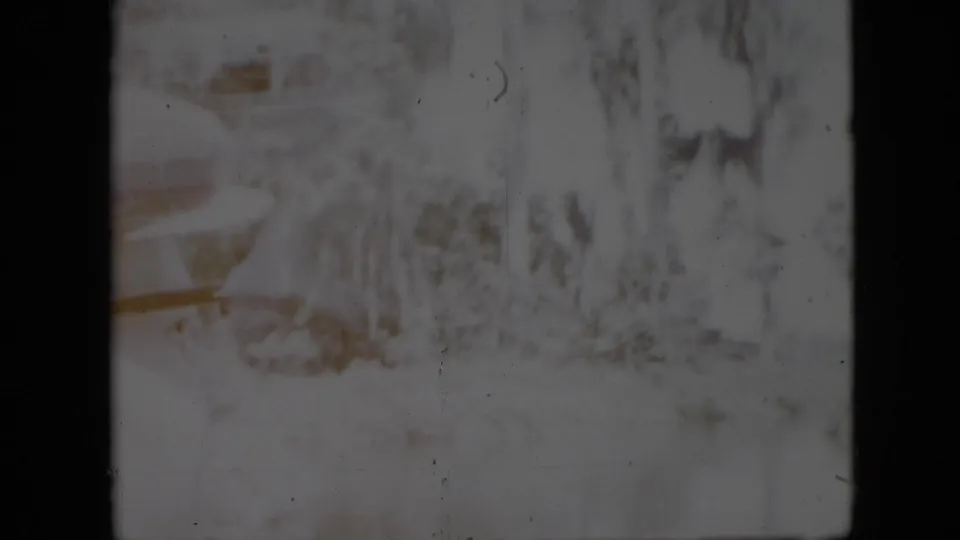 1958 Pennsylvania home-movie frame showing a pale riverbank with trees and brush viewed through a dark interior window or gate edge.