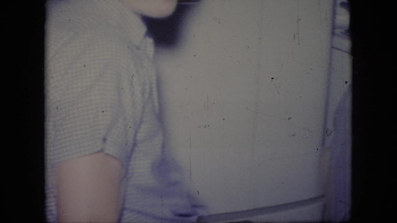 Adult man in a light striped shirt standing beside a white refrigerator.