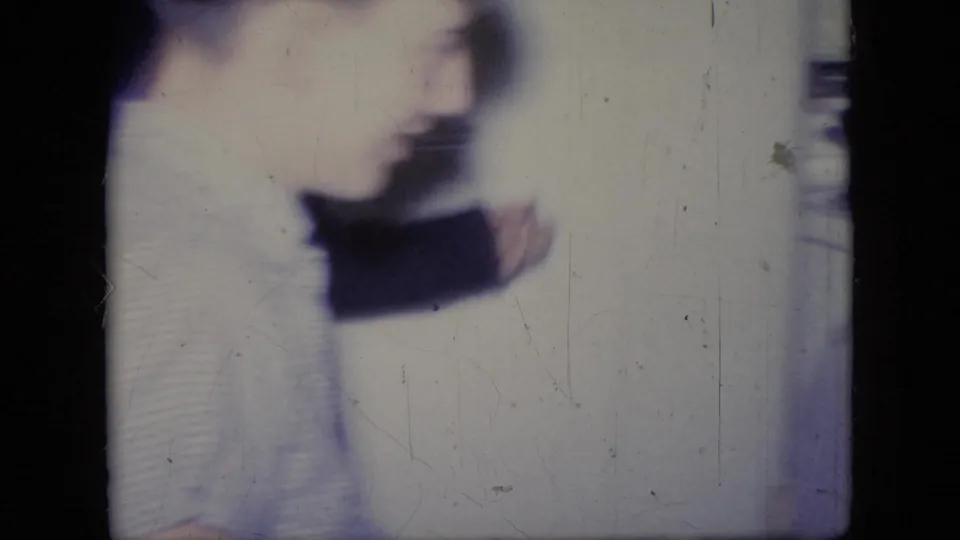 A blurred adult woman, likely in a light skirt and dark sweater, moves across an indoor Philadelphia home-movie scene from 1964.