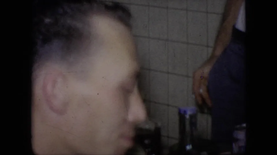 A close, softly focused profile of an adult man appears beside a tiled wall in the 1964 Philadelphia home-movie interior.