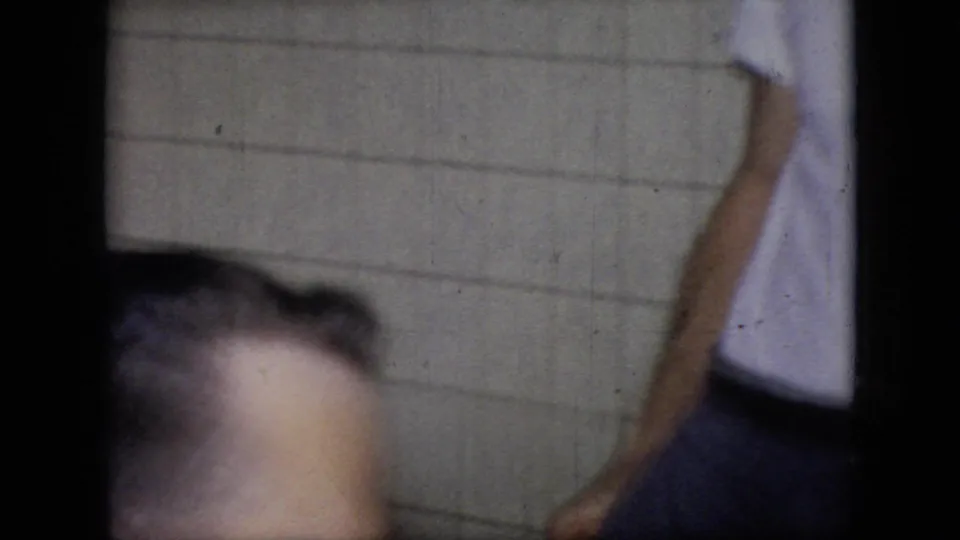 An adult man is partly framed near the bottom while another person stands by a tiled wall in a 1964 Philadelphia family interior.