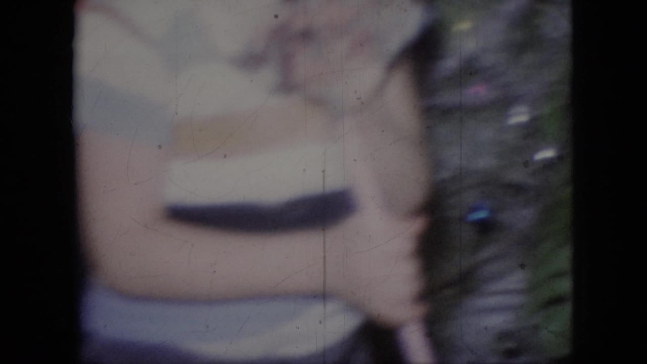 Soft 1964 Philadelphia 8mm frame showing a close, blurred visitor view of a striped shirt and hand near a glass barrier or enclosure edge.