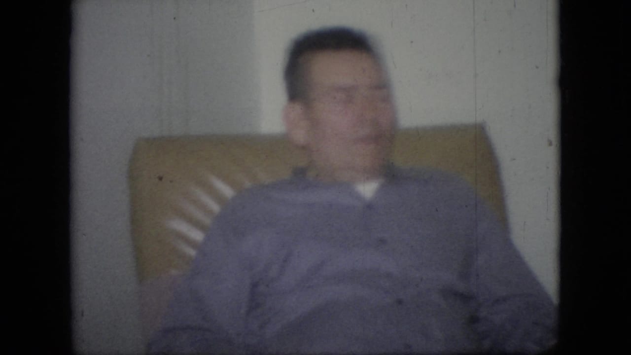 Adult man seated in a tan chair with soft focus and visible film wear.
