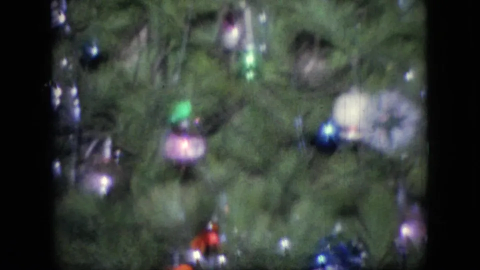 The camera has panned to a decorated Christmas tree with green branches, small colorful ornaments, and lights in a 1964 home interior.