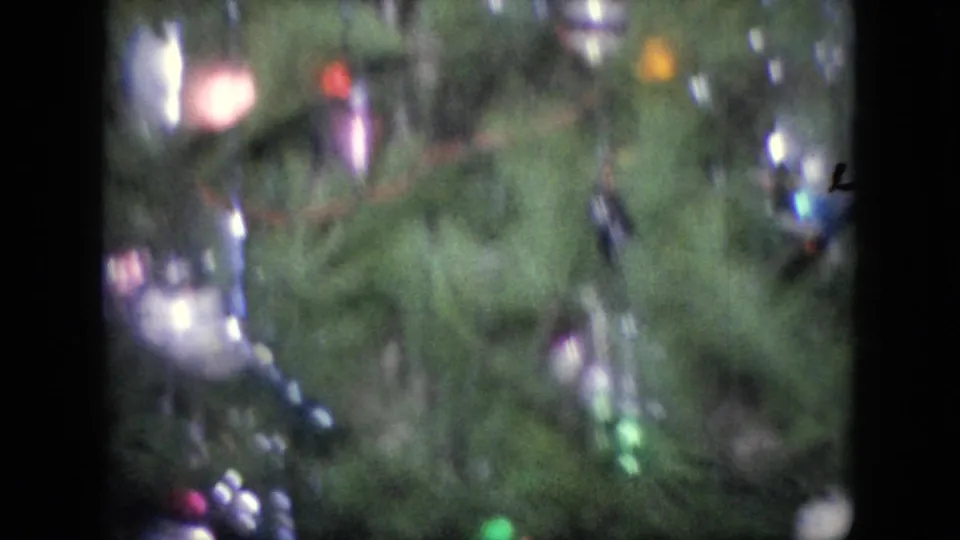 A soft handheld frame shows the Christmas tree decorations, including colored baubles and lights, during the pan across the private holiday interior.