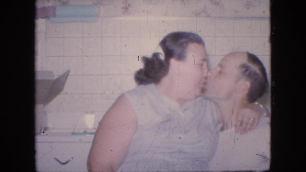Woman and man seated close together in a kitchen as they kiss.