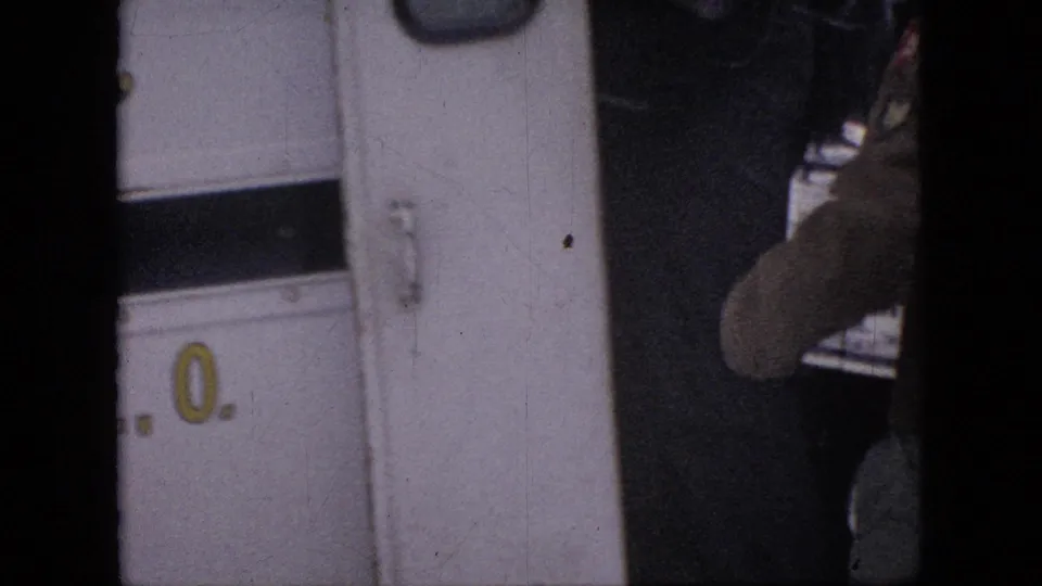 A partially visible person stands near or opens a white door in 1964 Philadelphia home-movie footage, with the frame cropped tightly and dark film borders visible.