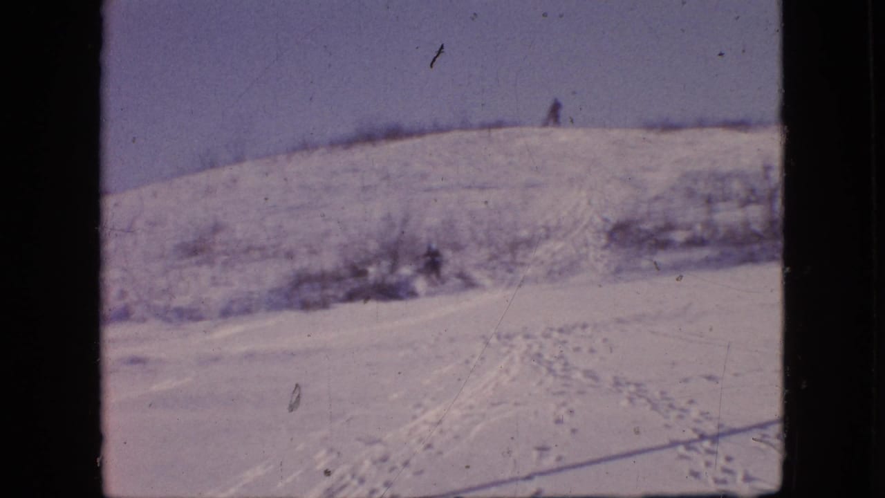 A snowy Philadelphia hillside in 1964, supported by metadata, with footprints and sled tracks leading across the slope and a distant bundled figure near the crest.