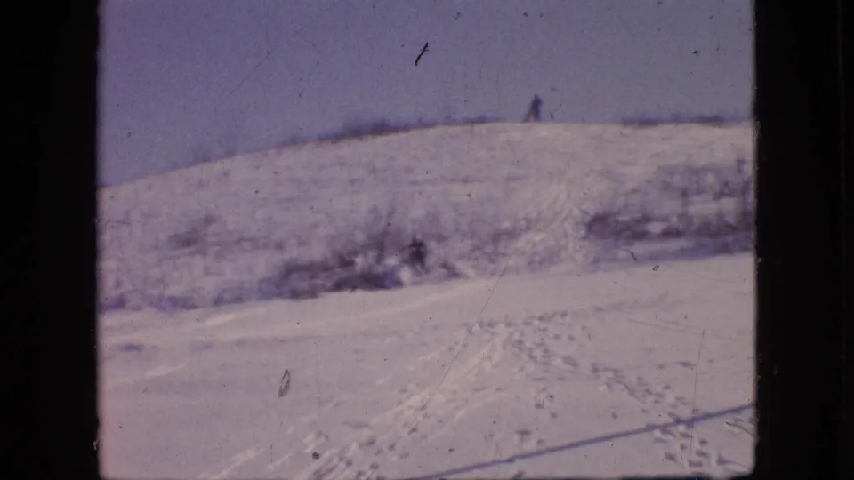 A snowy Philadelphia hillside in 1964, supported by metadata, with footprints and sled tracks leading across the slope and a distant bundled figure near the crest.
