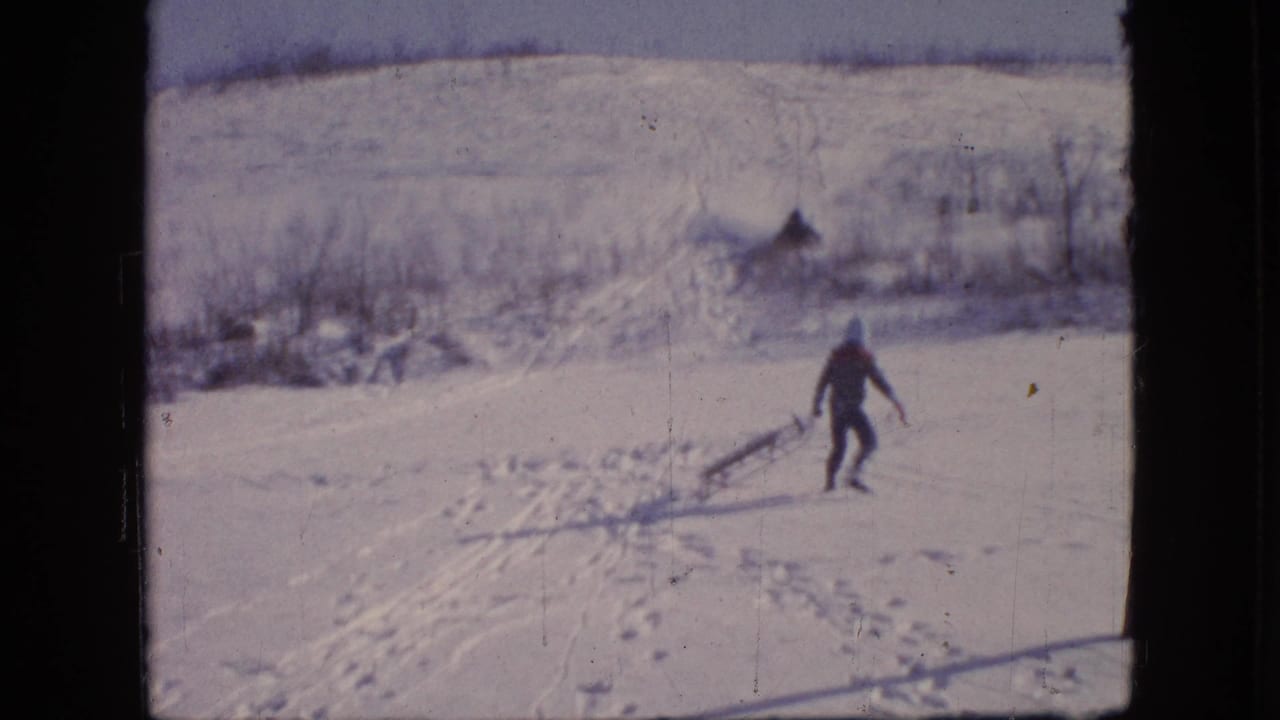 Bundled person pulling a sled across a snowy hill with brush in the background.