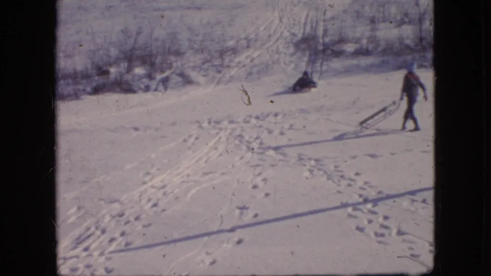Two bundled figures appear on a snowy Philadelphia hillside, one pulling a sled while the other sits or slides low on the slope.