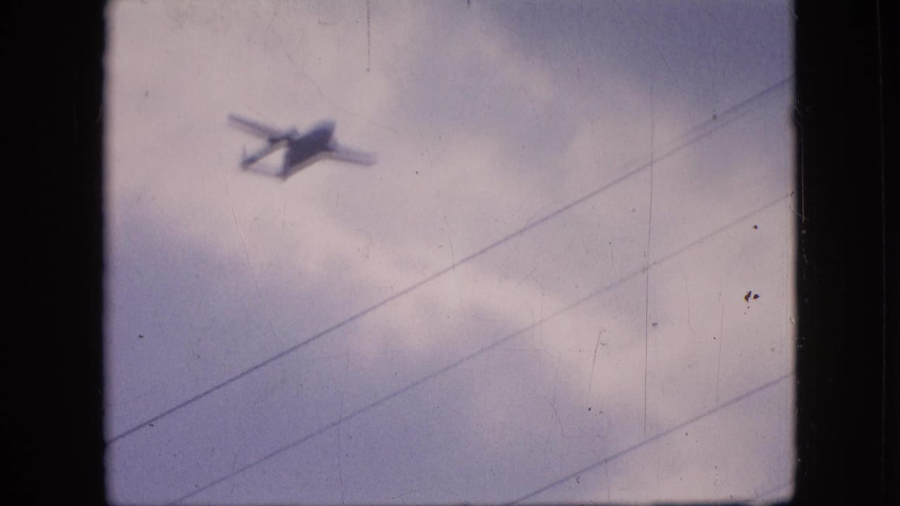 Twin-engine aircraft silhouette near the top of a cloudy frame with wires below.