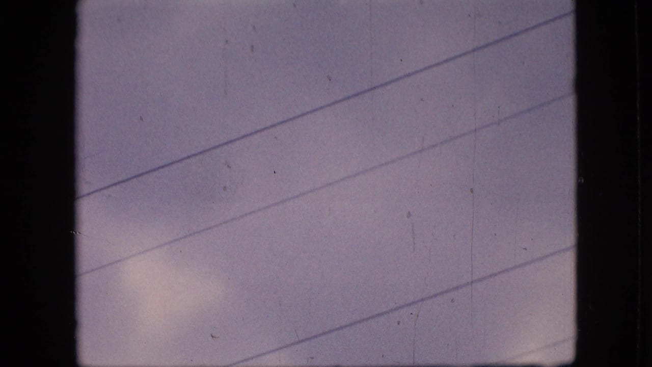 1964 Philadelphia home-movie frame showing a cloudy pastel sky crossed by diagonal overhead electric wires and framed by dark 8mm gate edges.