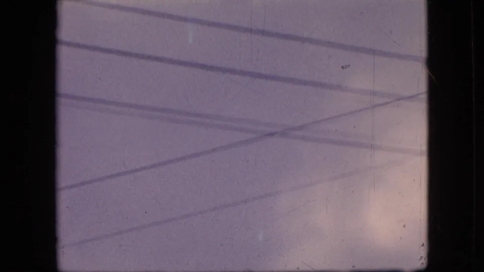 1964 Philadelphia 8mm frame with soft clouds and multiple overhead wires running diagonally and horizontally across the sky.