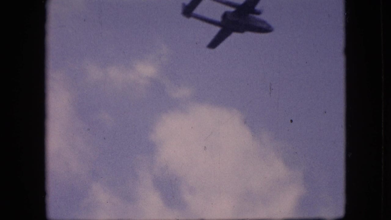 Dark aircraft silhouette partly visible near the top of a cloudy blue sky frame.