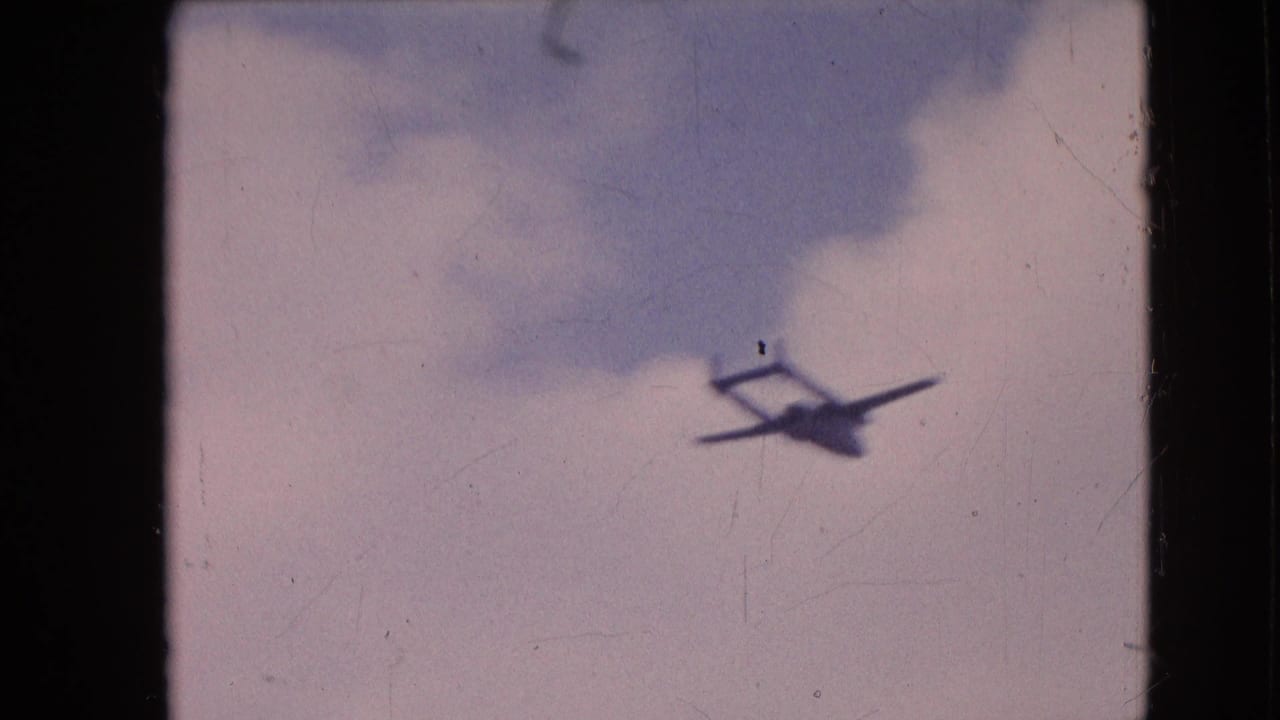 Small aircraft appears in a cloudy sky on soft, faded 8mm footage from the supplied 1964 Philadelphia home-movie clip.