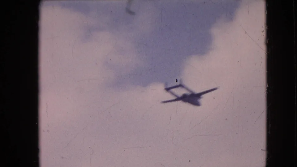 Small aircraft appears in a cloudy sky on soft, faded 8mm footage from the supplied 1964 Philadelphia home-movie clip.