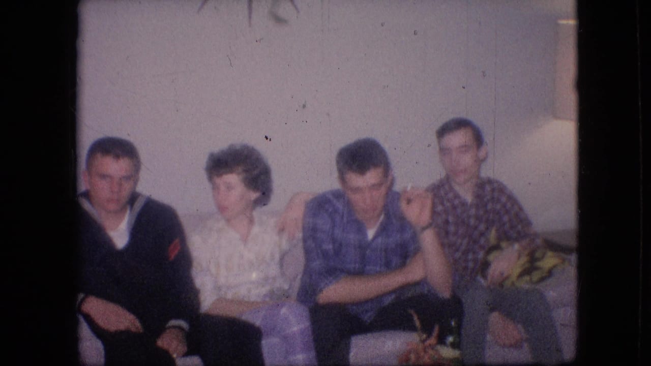 1964 Philadelphia home-movie frame showing three men and one woman seated on a light couch, with the group facing forward and toward one another in a private living room.
