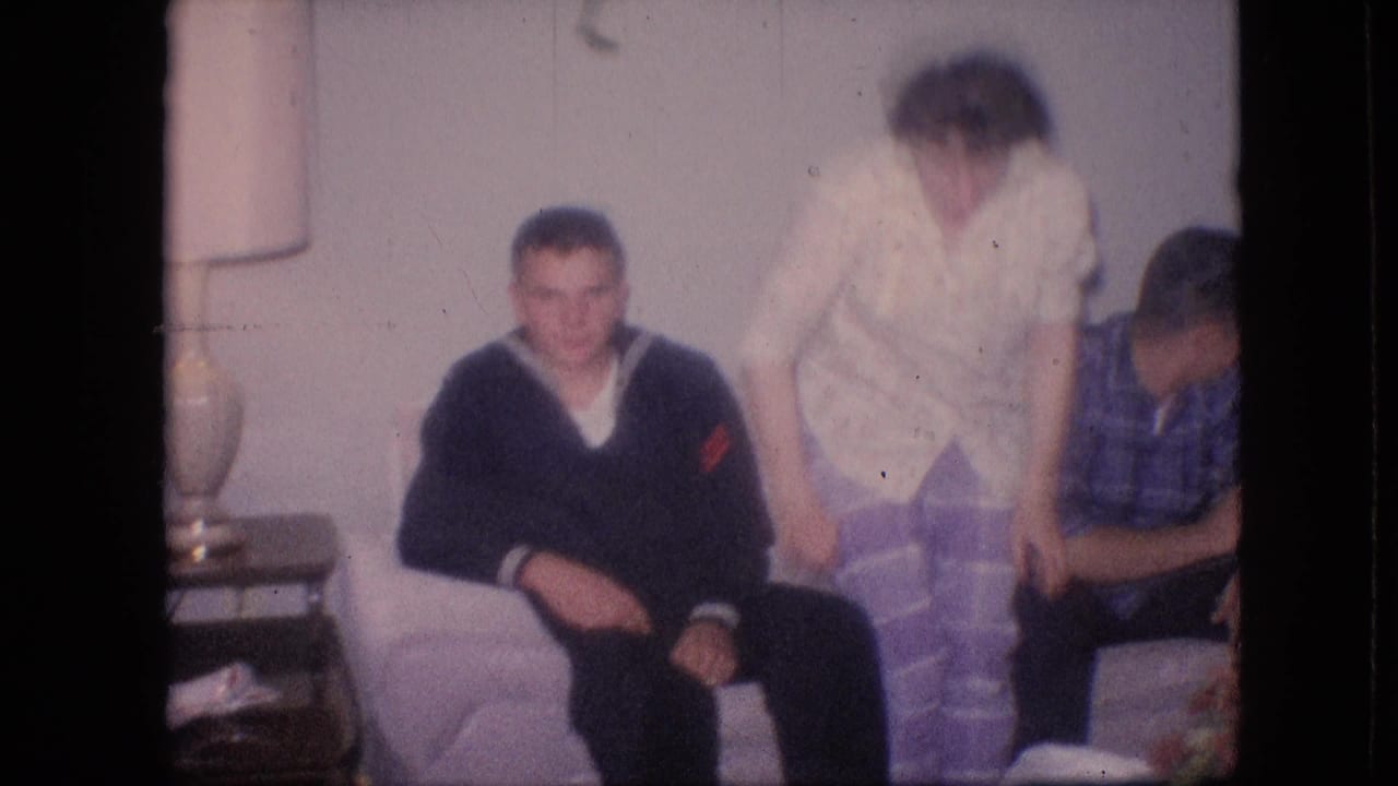 Woman in light purple pants stands near seated adults on a couch.