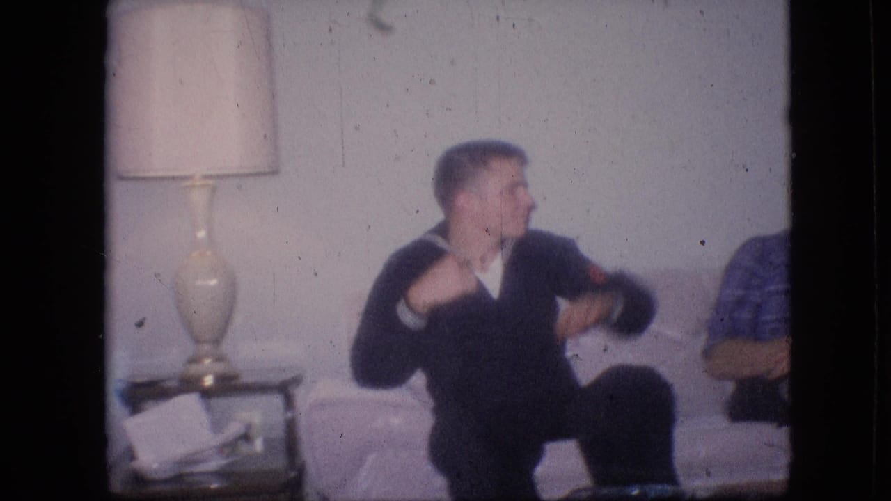 Young man in dark top sitting on a sofa beside a table lamp.