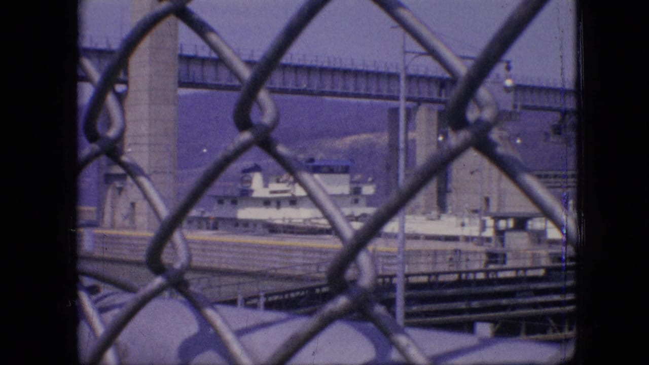 Docked vessel and bridge framed behind chain-link fencing.