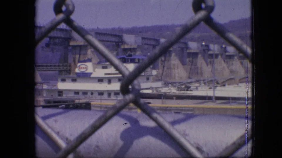 A closer 1964 Philadelphia frame shows the boat's cabin and hull passing through the lock, with fence links and a large pipe or rail in the foreground.