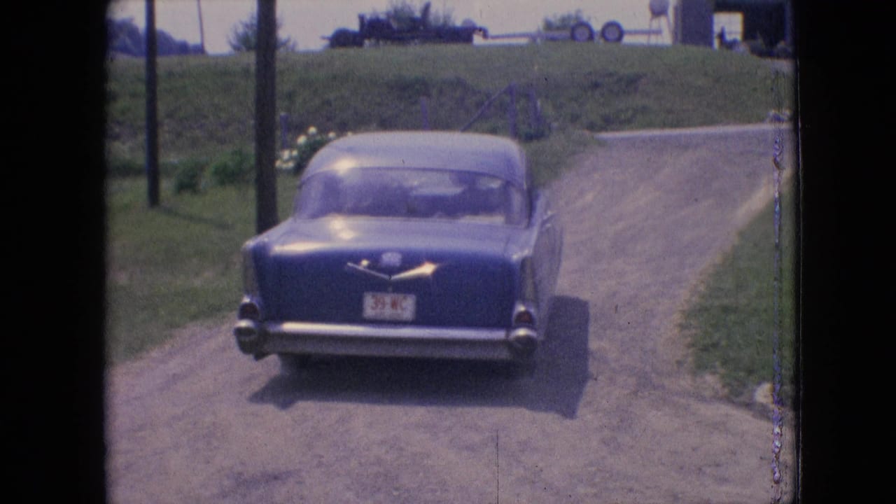 A blue mid-century sedan drives away on a rural dirt driveway in footage supplied as 1964 Philadelphia, Pennsylvania home-movie material.