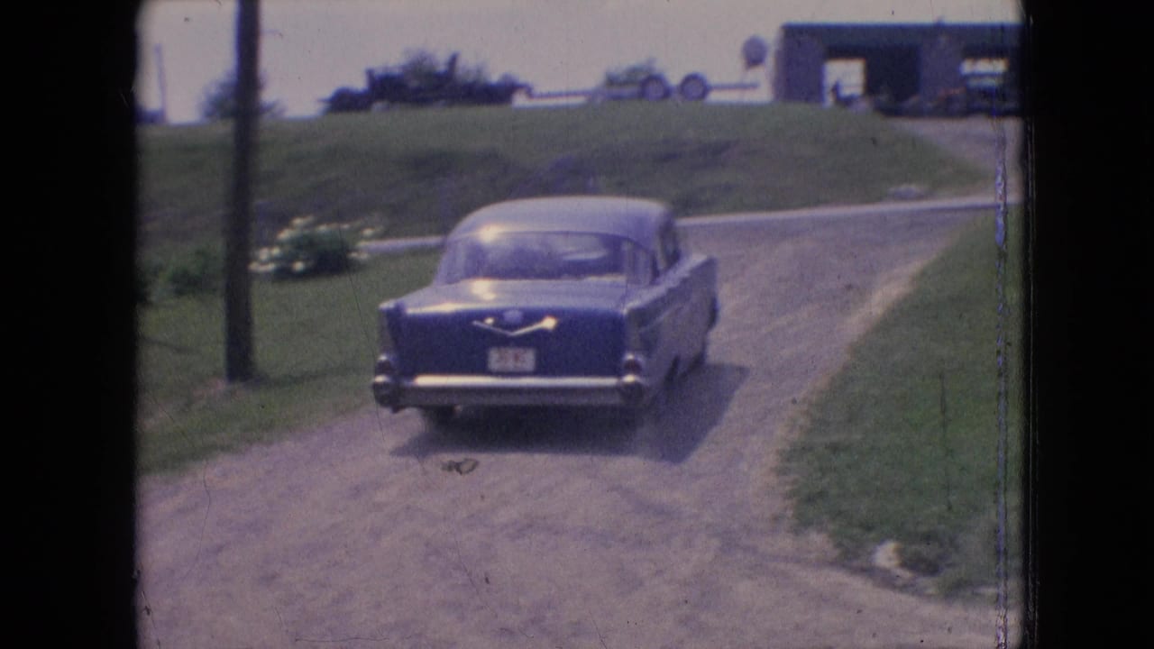 Blue sedan farther down a dirt road near grass and poles.