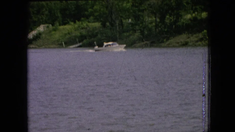 Metadata-supported 1964 Philadelphia-area home-movie frame showing a small boat near the wooded shore across a lake or broad river.