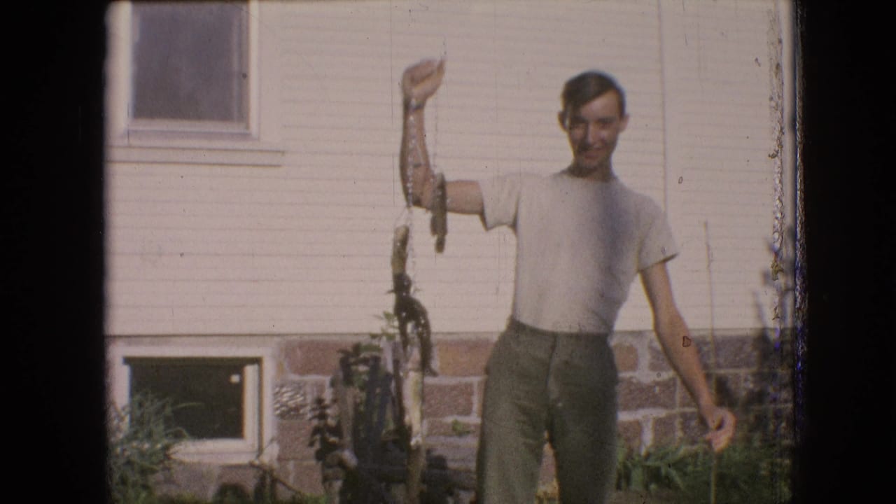 Young man raises a line of fish in bright sun in front of a house exterior.