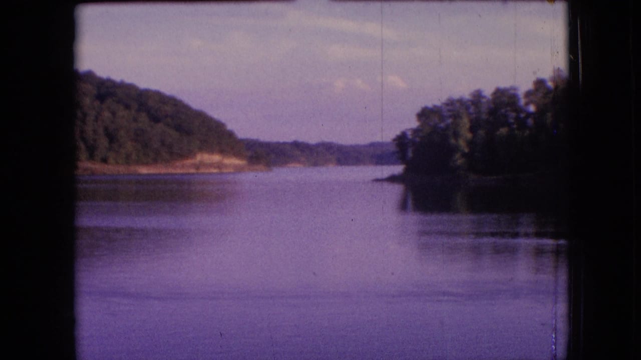 1964 metadata-supported 8mm frame showing a quiet lake corridor near Philadelphia, Pennsylvania, framed by wooded banks and a distant shoreline beneath a soft sky.