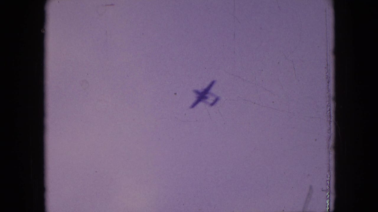 Small aircraft silhouette in a faded sky from 1964 Philadelphia home-movie footage, with visible 8mm grain and frame edges.