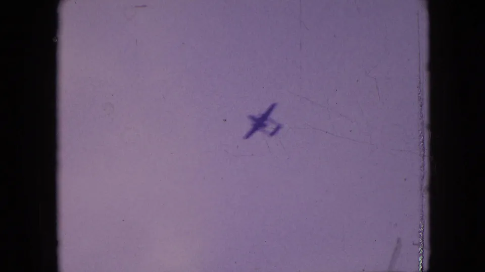 Small aircraft silhouette in a faded sky from 1964 Philadelphia home-movie footage, with visible 8mm grain and frame edges.