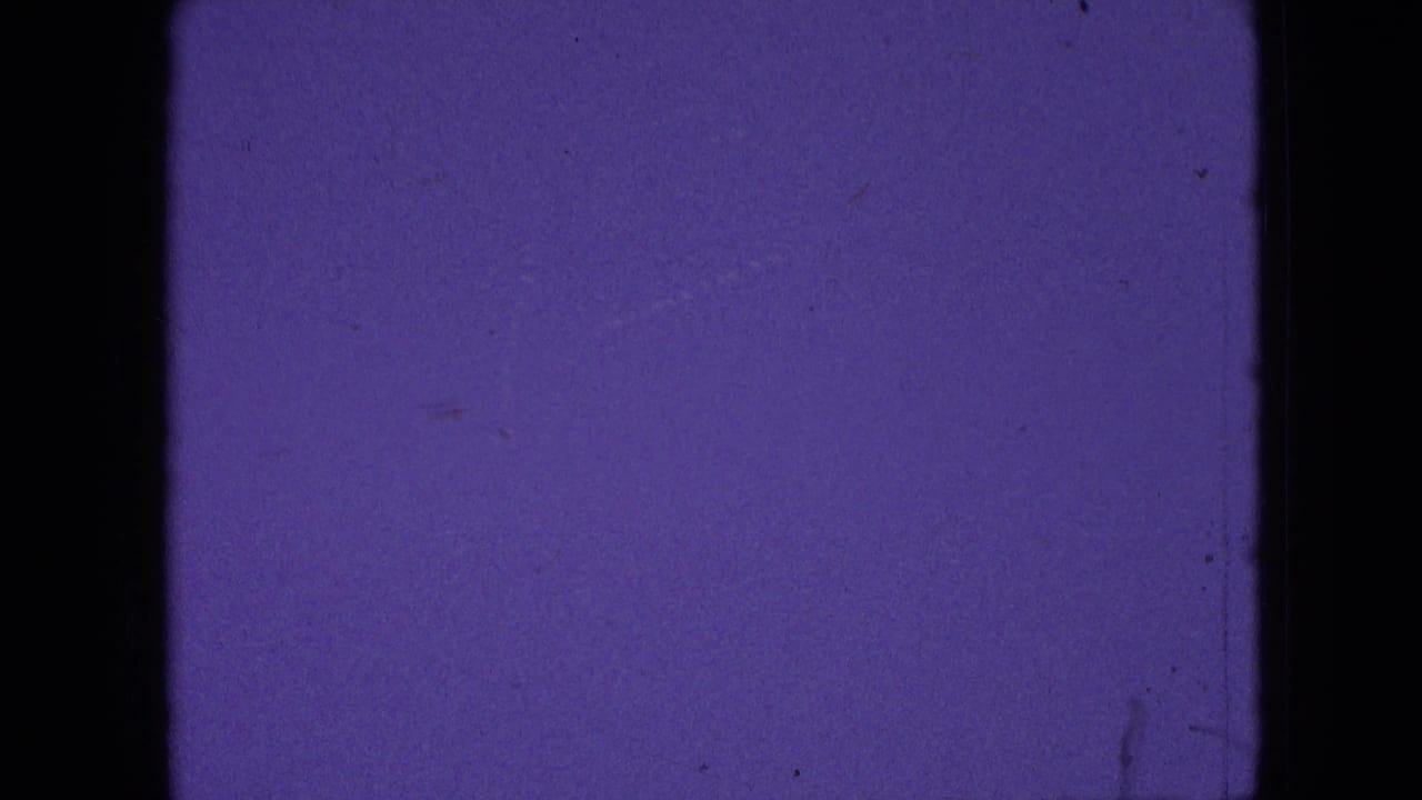 Purple-tinted 8mm frame from the 1964 Philadelphia-area clip with film edges, dust, and minimal visible scene detail before the hillside view appears.