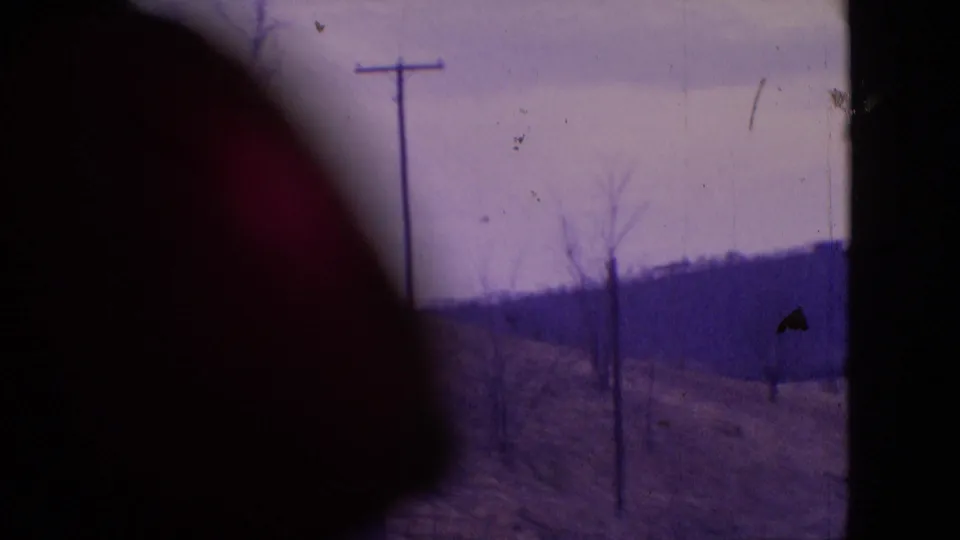 1964 Philadelphia-area 8mm frame showing the hillside telephone pole and bare trees partly blocked by a dark foreground obstruction, with distant hills and aged film texture visible.