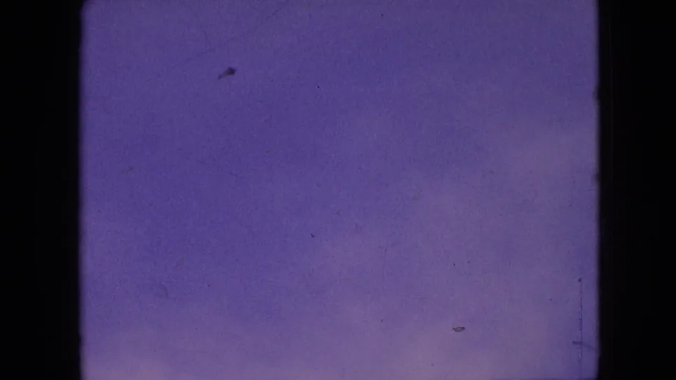 1964 Philadelphia home-movie frame of open purple sky with faint specks and visible 8mm dust, scratches, and edge wear.