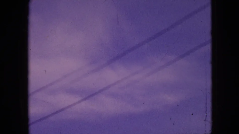 1964 Philadelphia home-movie frame showing purple sky with diagonal overhead lines or wires, faint clouds, and visible film grain and scratches.