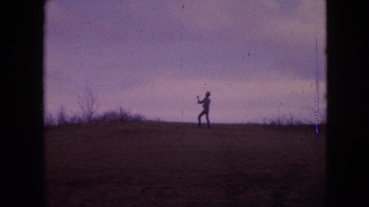 1964 8mm home-movie frame from the supplied Philadelphia metadata showing a distant silhouetted person on an open-field ridge under a purple-tinged sky.