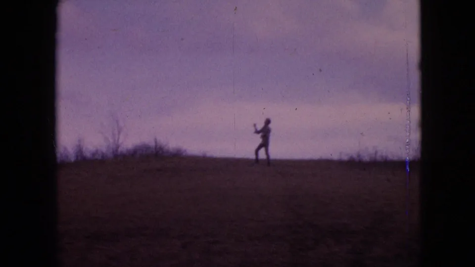 1964 8mm home-movie frame from the supplied Philadelphia metadata showing a distant silhouetted person on an open-field ridge under a purple-tinged sky.