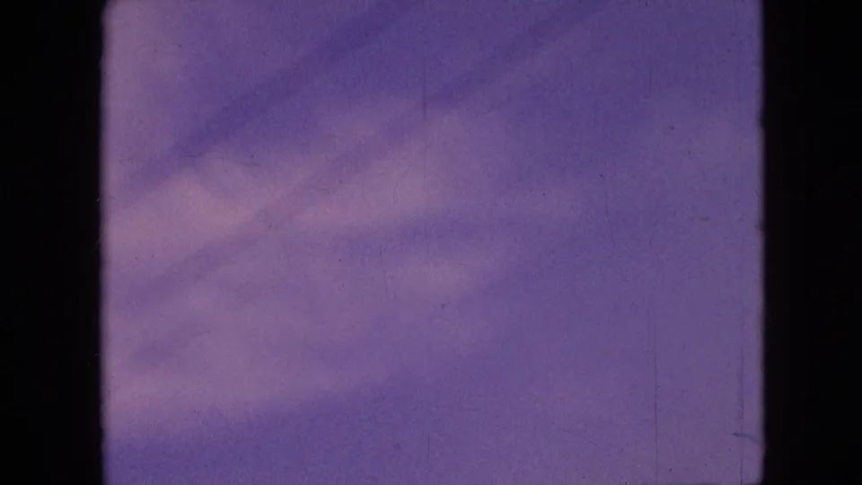 Faded 8mm frame showing a mostly empty purple-blue sky above a low field edge, with the figure no longer clearly visible in the crop.