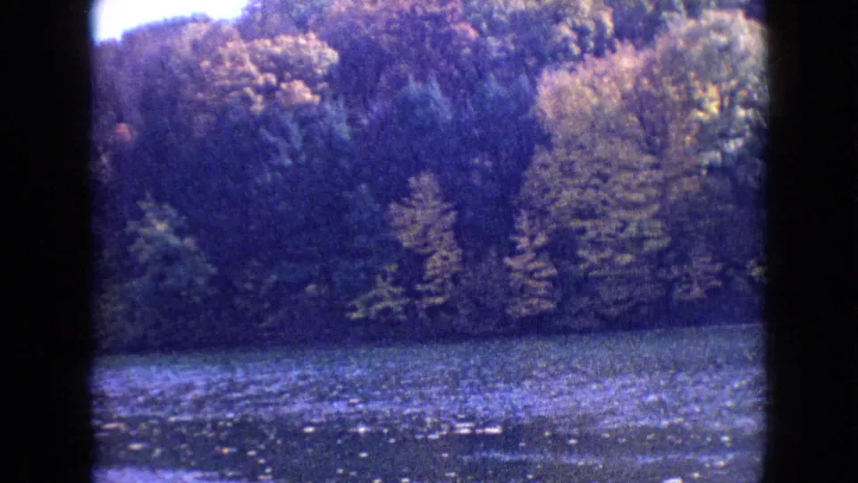The frame holds on a Philadelphia lake surface and dense fall-colored trees, with the home-movie camera pointed across the water.