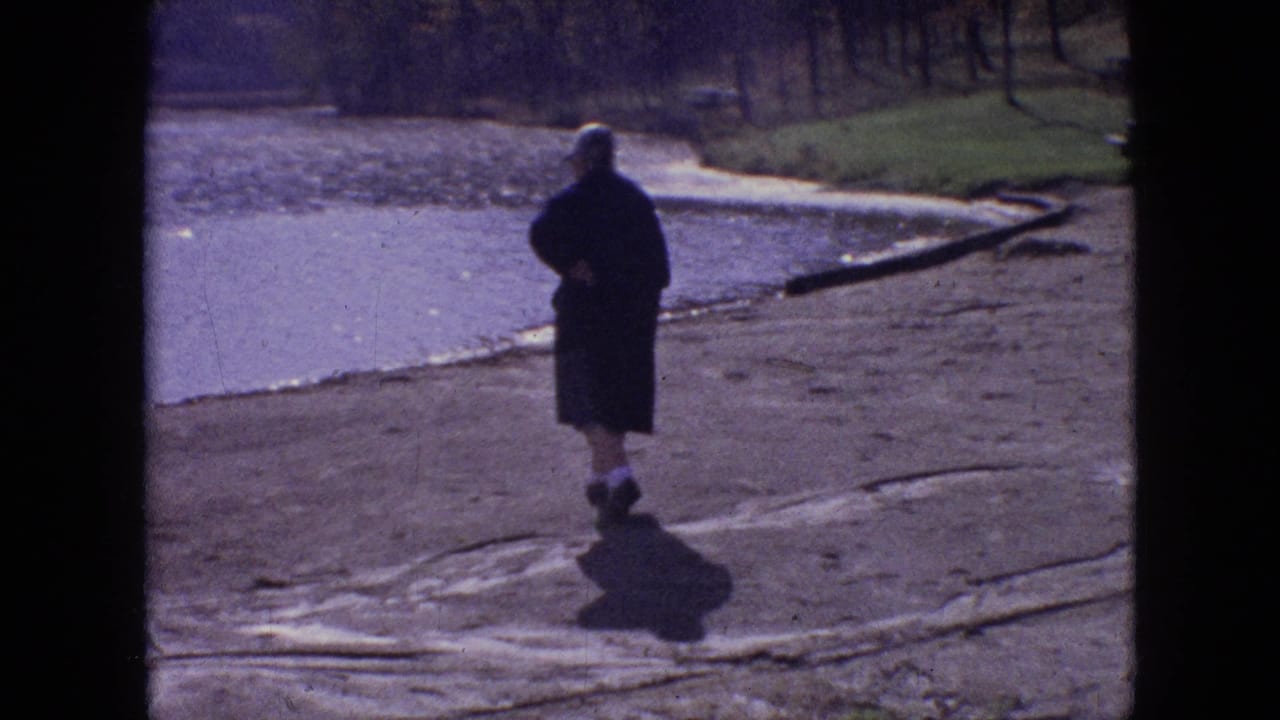 Woman continues away from the camera near the water's edge on a bare bank.
