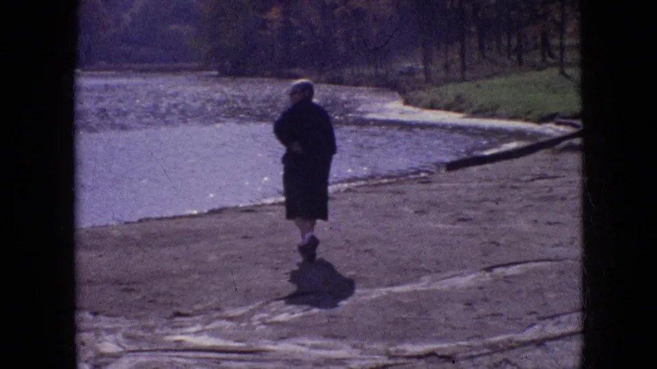 A rear-view frame shows the woman on the sloped exposed bank, with calm water to the left and a wooded bank in the distance in the supplied Philadelphia setting.