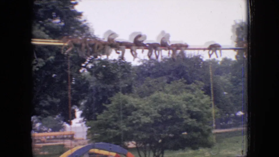 A group of baboons clusters along an elevated pole in the 1964 Philadelphia zoo footage, with leafy trees, railings, and the edge of the stone climbing area below.